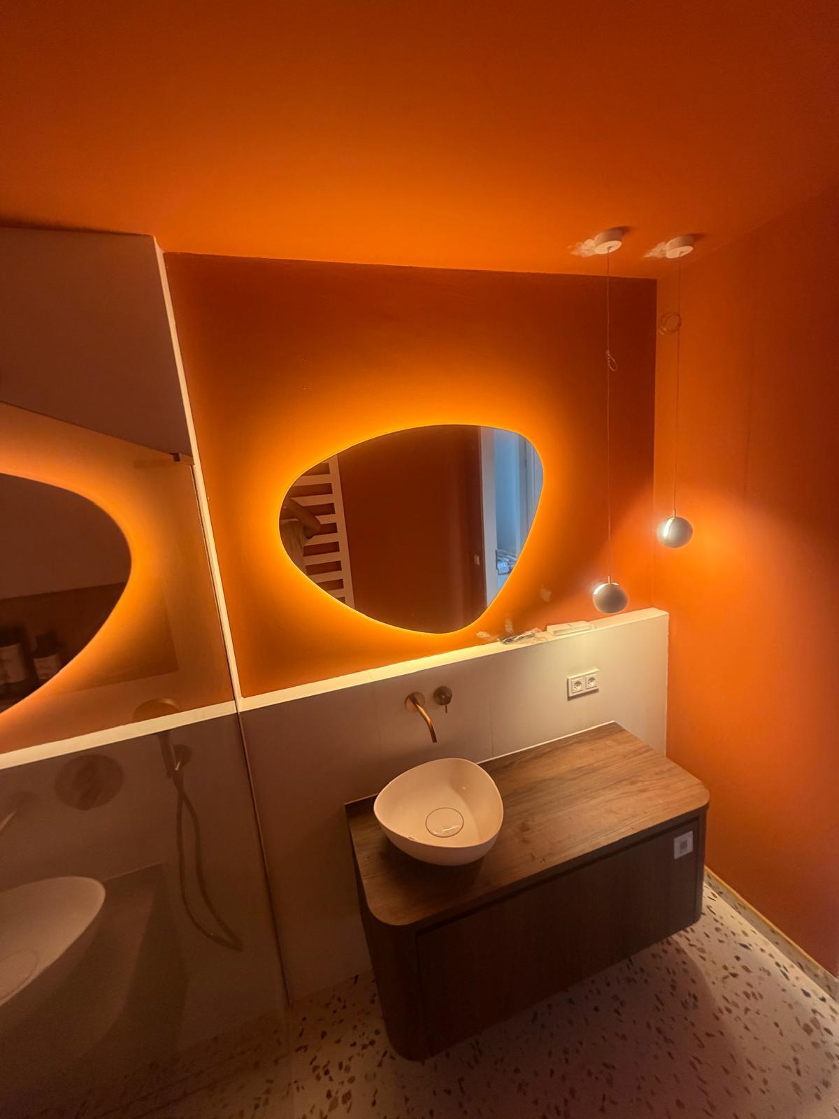 Badkamer met oranje wand, verlichte spiegel en terrazzo vloer